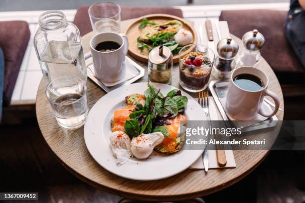 brunch at the cafe with salmon and poached egg on avocado toast, side view - breakfast restaurant stock pictures, royalty-free photos & images