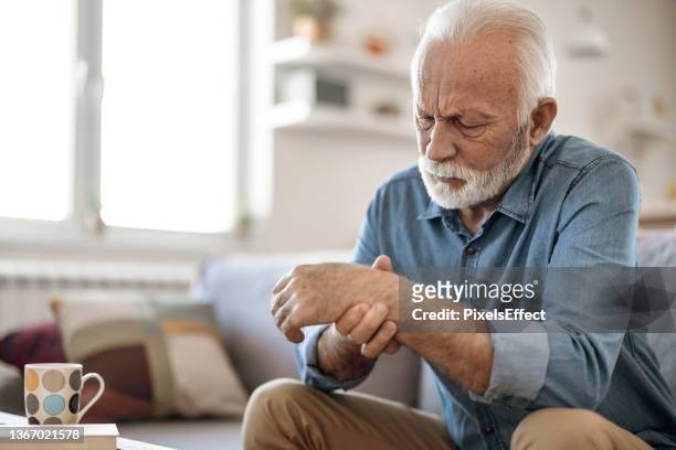 hombre mayor masajea su mano con dolor de muñeca - hold wrists fotografías e imágenes de stock