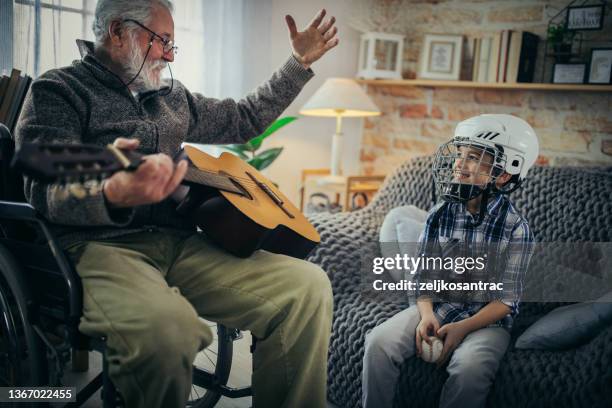 grandfather in wheelchair with his grandson spend time together at home - guitar & medical books stock pictures, royalty-free photos & images