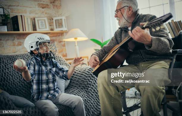 grandfather in wheelchair with his grandson spend time together at home - guitar & medical books stock pictures, royalty-free photos & images