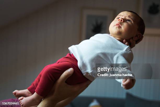 side view of newborn being held by his father in the living room. - baby father hug side stock pictures, royalty-free photos & images