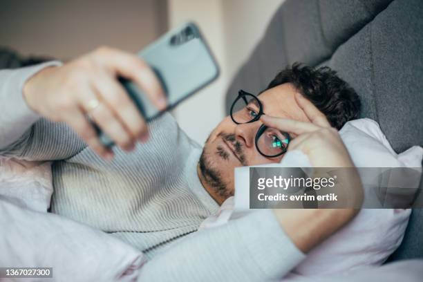 kranker mann, der sein smartphone überprüft, wenn er sich im bett ausruht - cellphone cancer illness stock-fotos und bilder
