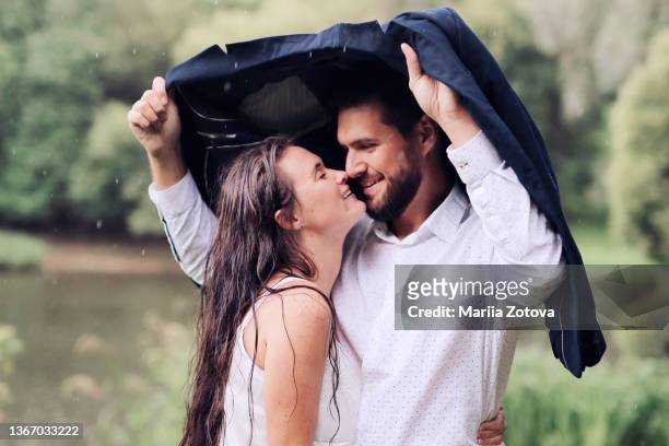 a beautiful young couple in love kissing in the rain in a summer park - couples kissing shower photos et images de collection