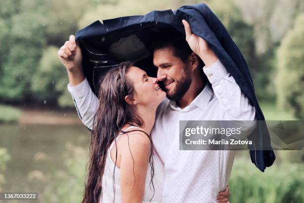 a beautiful young couple in love kissing in the rain in a summer park - rain couple stockfoto's en -beelden