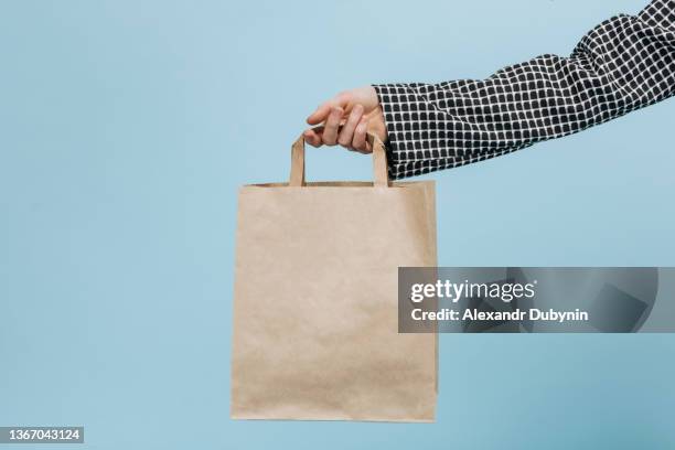 person's woman's hand holds a craft eco bag with goods on a blue background. delivery concept - craft market stock pictures, royalty-free photos & images