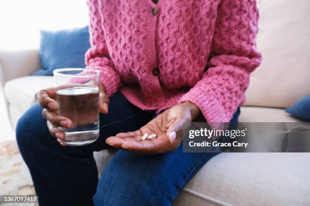 woman holds capsules and glass of water - gelule photos et images de collection