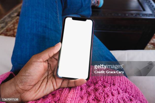 woman sits on couch holding smart phone with blank screen - black hand holding phone stock-fotos und bilder