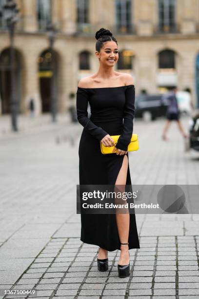 Lena Mahfouf aka Lena Situations wears a black long sleeves / shoulder-off slit midi dress, a yellow shiny leather handbag from Valentino, black...