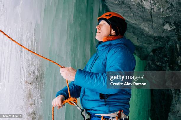 a man belays his climbing partner from inside an ice cave - kamloops fotografías e imágenes de stock