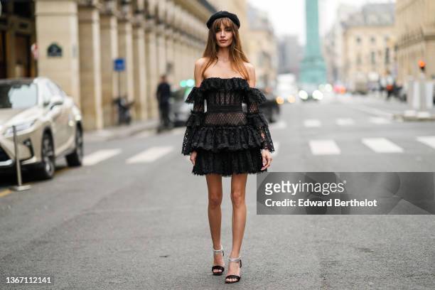 Mara Lafontan wears a black felt / wool beret hat, a black lace print pattern shoulder-off / puffy long sleeves ruffled dress, a black ribbed velvet...