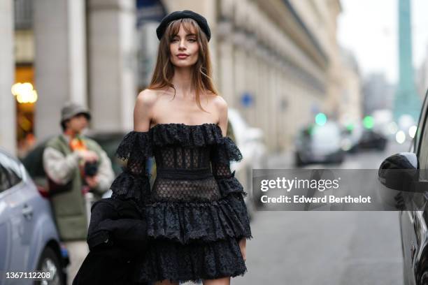 Mara Lafontan wears a black felt / wool beret hat, a black lace print pattern shoulder-off / puffy long sleeves ruffled dress, a black ribbed velvet...