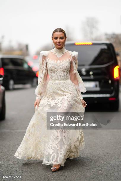 Veronica Ferraro wears a gold and diamond large pendant earrings, a white tulle and embroidered lace print pattern high neck / puffy sleeves / long...