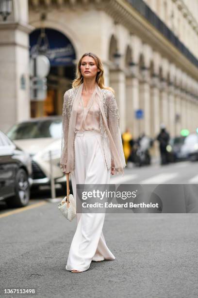 Chloe Lecareux wears a beige tulle with diamond embroidered pattern kimono / jacket, a beige transparent silk shirt, high waist white large flowing...