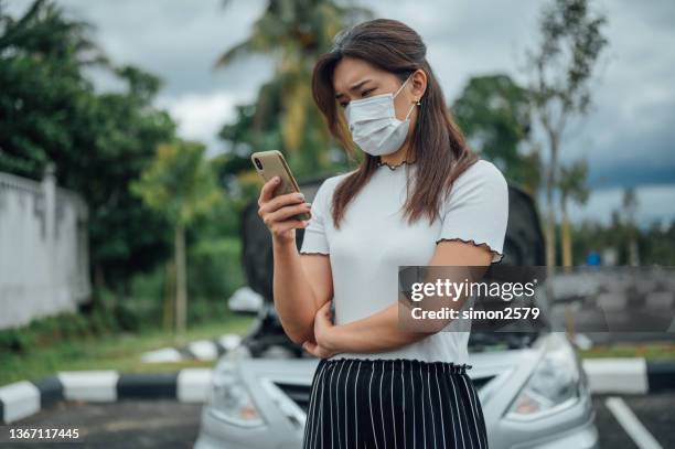 young asian woman wearing protective face mask and using smart phone asking for assistance near her car broken down on the road side - overheated stock pictures, royalty-free photos & images