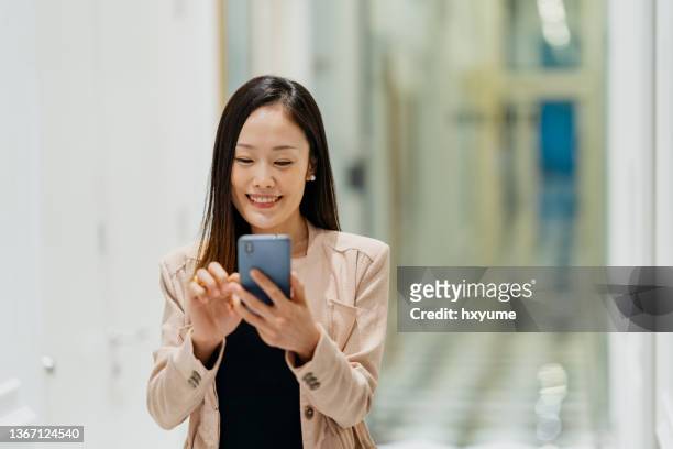 junge asiatische geschäftsfrau mit smartphone im bürokorridor - gaming mobile stock-fotos und bilder