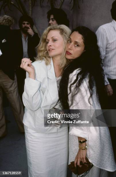 American actress Beverly D'Angelo and Brazilian actress Sonia Braga pose cheek-to-cheek, both dressed in white, circa 1990.