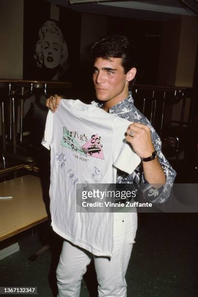 American actor Brian Bloom holding a t-shirt with 'Driver's Ed: The Movie' printed on the chest, attends the announcement of the NBC television movie...