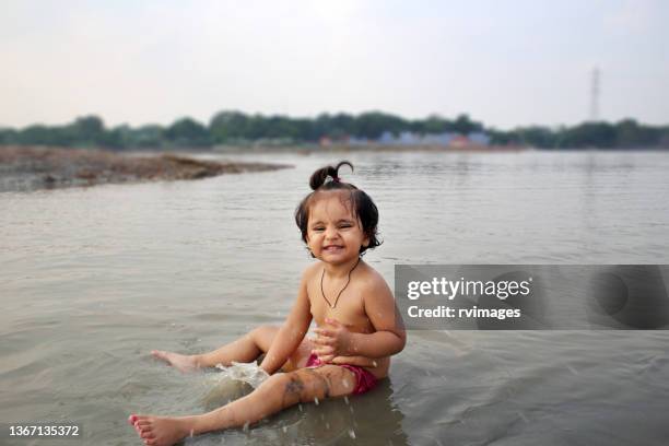 cheerful baby girl enjoying at the edge of yamuna river, delhi, india - no clothes girls stock pictures, royalty-free photos & images