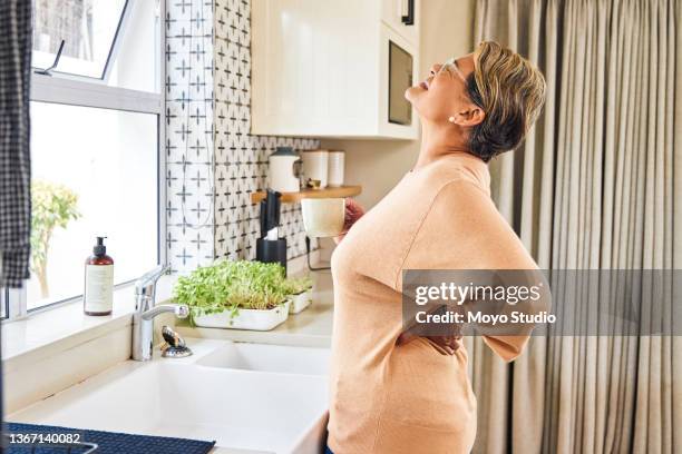 cropped shot of an attractive senior woman holding her back in pain while standing in the kitchen at home - back pain 個照片及圖片檔