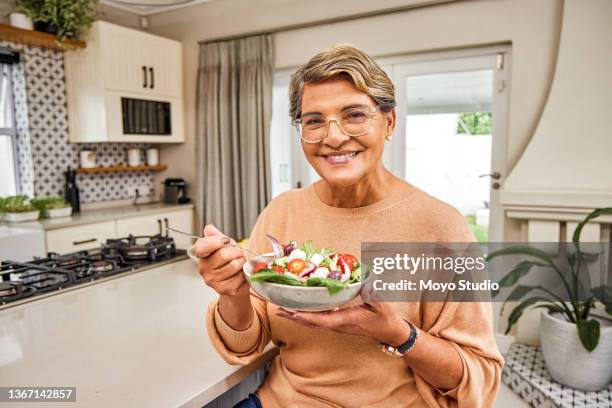 cropped portrait of an attractive senior woman enjoying a bowl of salad while standing in her kitchen at home - paleo diet stock pictures, royalty-free photos & images