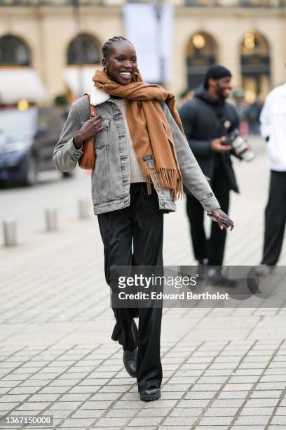 Model wears a brown cashmere fringed scarf from Rag & Bone, a gray faded denim jacket with sheep interior, black large flowing suit pants, a brown...