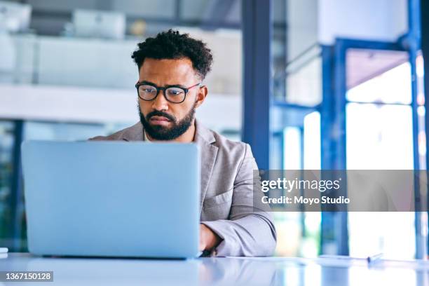 shot of a young businessman using a laptop in a modern office at work - stern stock pictures, royalty-free photos & images