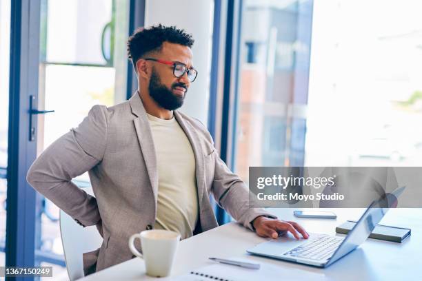 foto de un joven empresario que sufre de dolor de espalda mientras trabaja en una oficina moderna en el trabajo - back pain fotografías e imágenes de stock