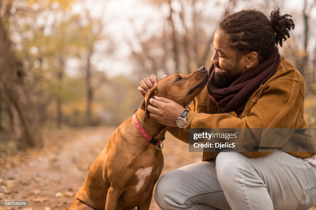 Happy young African American man petting his dog outdoors in nature.