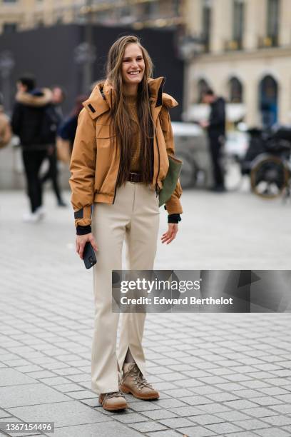 Guest wears a brown turtleneck wool braided pullover, a pale brown hoodie rain coat, a brown shiny leather belt, beige slit / split pants, brown...
