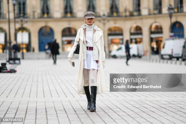 Guest wears a beige with burgundy and black checkered print pattern beret cap, gold large earrings, a white wool ribbed turtleneck pullover, a white...