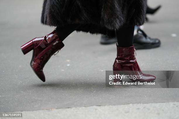 Guest wears a black long fur coat, black tight, burgundy shiny leather zipper block heels ankle boots, outside Elie Saab, during Paris Fashion Week -...