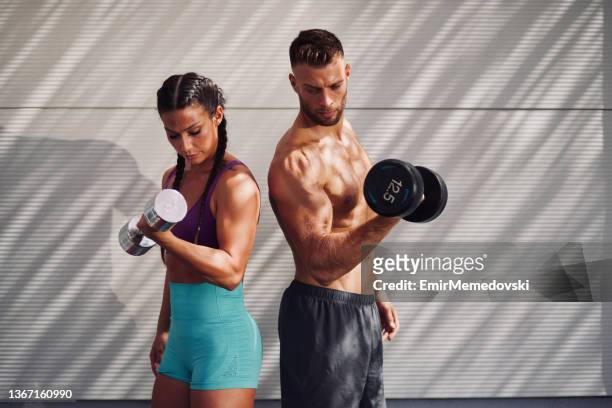 athletic couple pumping up muscles with dumbbells outdoors - slim stock pictures, royalty-free photos & images