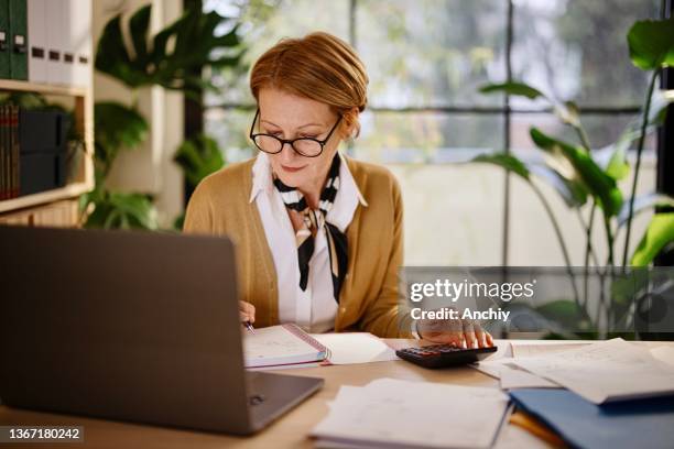 mature businesswoman calculating finances in an home office - generation x stock pictures, royalty-free photos & images