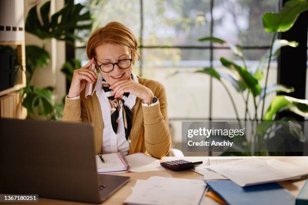 happy businesswoman using mobile and laptop while working at home - boekhouding stockfoto's en -beelden