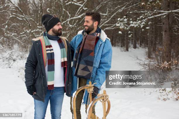 zwei männliche freunde amüsieren sich auf dem schnee mit einem schlitten - family sport winter stock-fotos und bilder