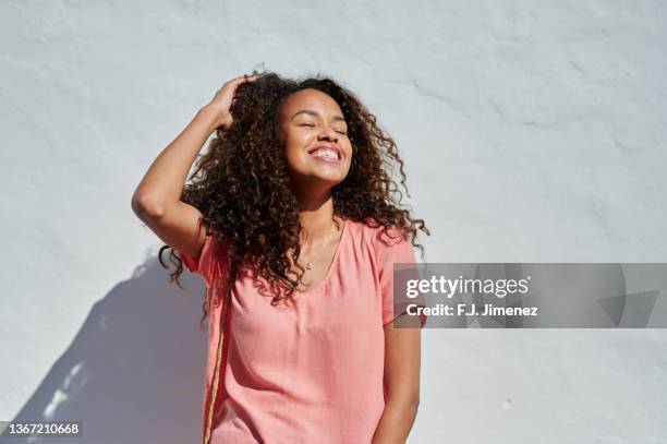 portrait of smiling woman with curly hair in front of white wall - sun on face stock pictures, royalty-free photos & images