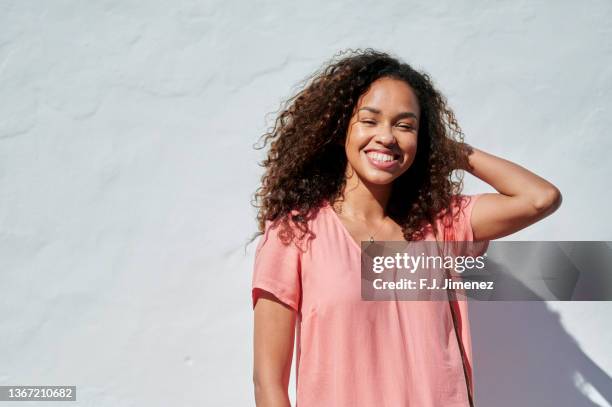 portrait of smiling woman with curly hair in front of white wall - african american young woman portrait white background stock-fotos und bilder