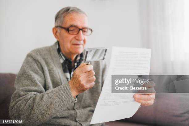 senior man holding an magnifying glass he uses to help him read because he suffers from wet macular degeneration. - macular degeneration stock pictures, royalty-free photos & images