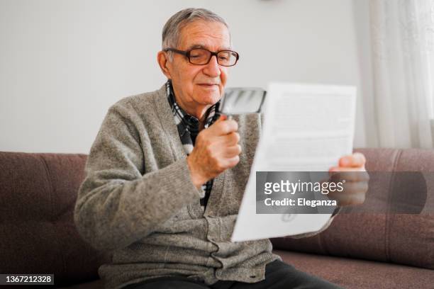 hombre mayor que sostiene una lupa que usa para ayudarlo a leer porque sufre de degeneración macular húmeda. - seat perilous fotografías e imágenes de stock
