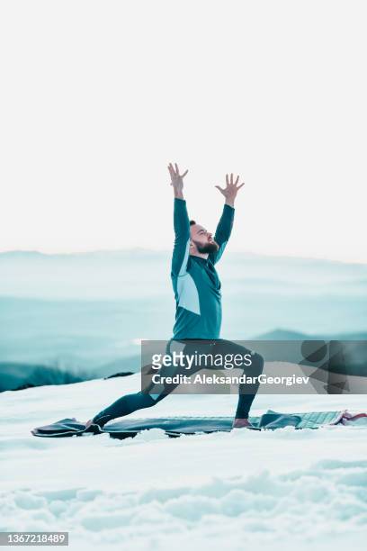 bärtiger mann, der krieger eine position im bergschnee macht - yoga in the snow stock-fotos und bilder
