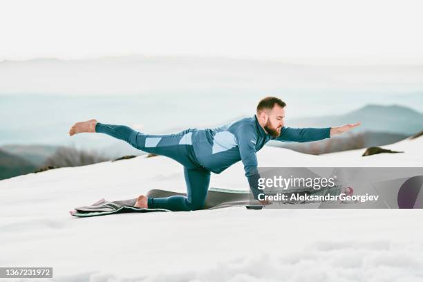 athletischer mann, der superman yoga pose im bergschnee übt - yoga in the snow stock-fotos und bilder