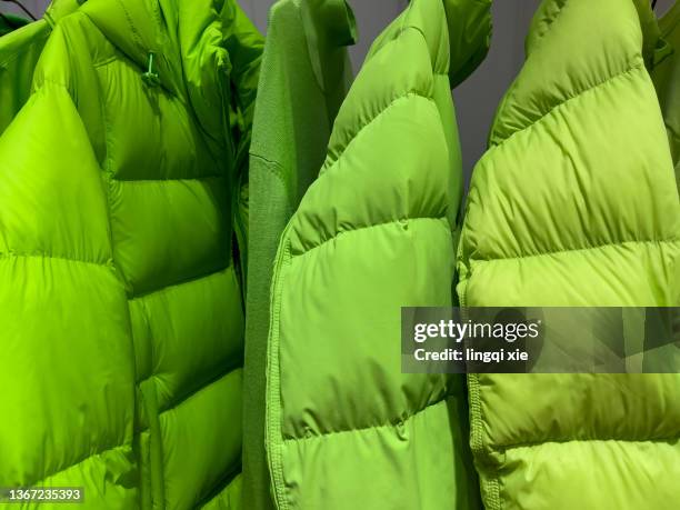 green down jacket hanging on clothes rack - down coat stock-fotos und bilder