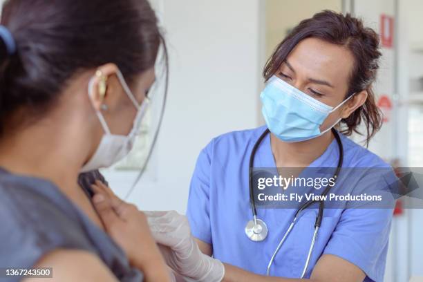 nurse of asian descent injects patient with covid-19 vaccine - aussie flu stock pictures, royalty-free photos & images