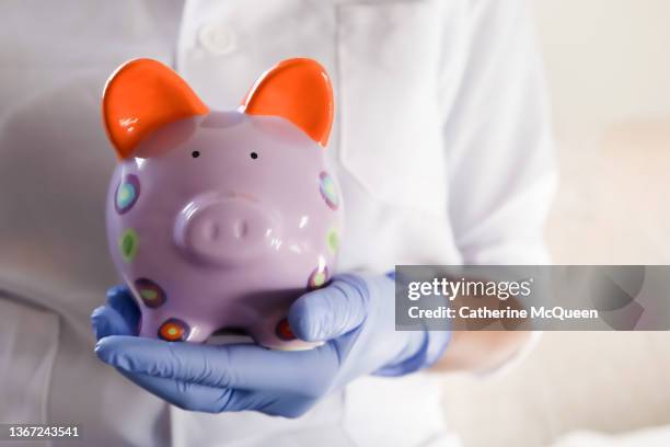 healthcare worker holding brightly colored piggy bank - patient protection and affordable care act stock pictures, royalty-free photos & images
