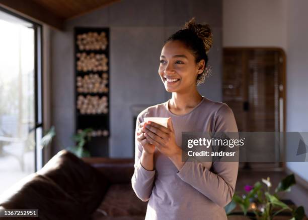 自宅で幸せな女性はコーヒーを飲みながら手を温める - tea hot drink ストックフォトと画像