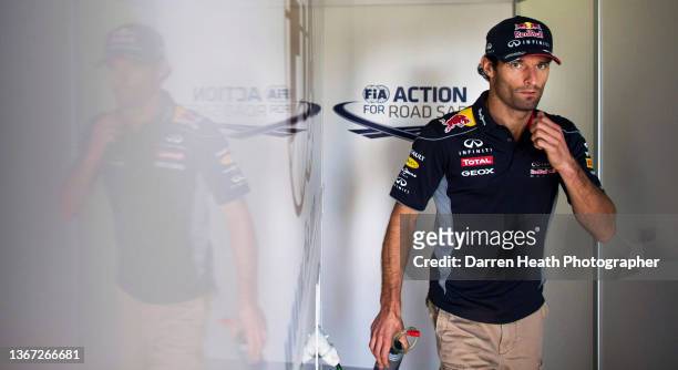 Australian Red Bull Racing Formula One team racing driver Mark Webber walking through the FIA pit lane garage while carrying a drink bottle and...