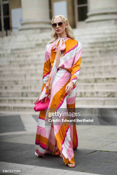 Miss Fame wears sunglasses from Loewe, a white / pale pink / orange / fuchsia stripped print pattern long flowing dress from Fendi, a gold belt, a...