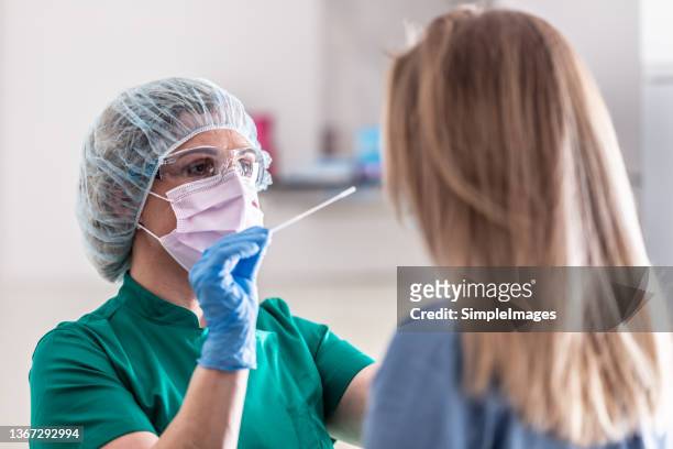 well-protected medical staff performs swab test for covid-19 to a young blonde female patient. - coronavirus stock pictures, royalty-free photos & images