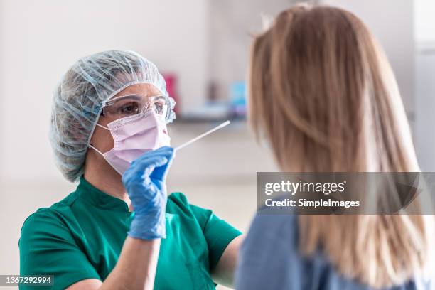 well-protected medical staff performs swab test for covid-19 to a young blonde female patient. - 科學實驗 事件 個照片及圖片檔