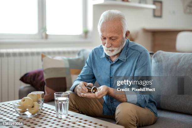 senior male taking pills - taking medication stockfoto's en -beelden